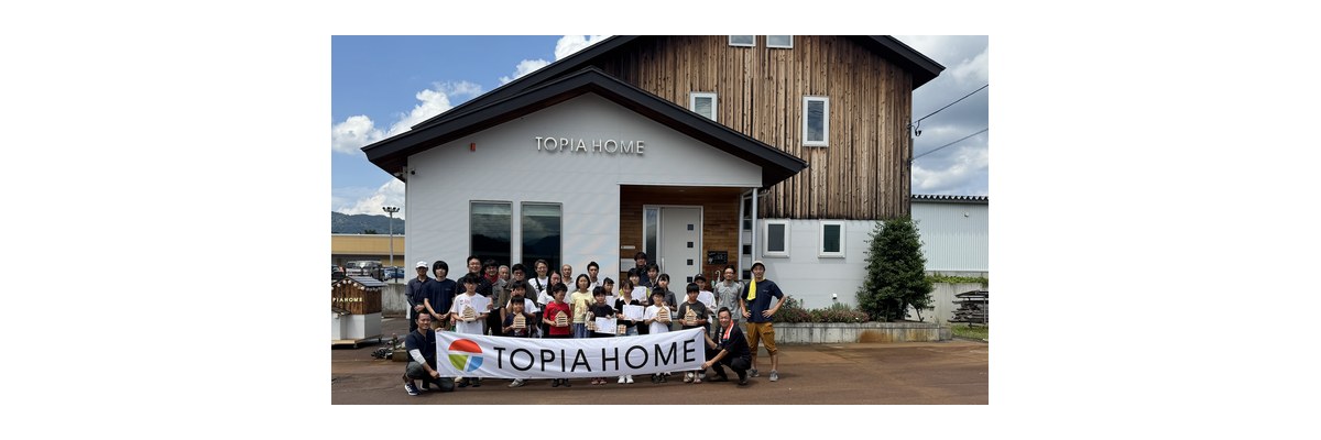 トピアホームの木工イベントで、作った木の家を手に社屋前に並ぶこどもたちとスタッフ