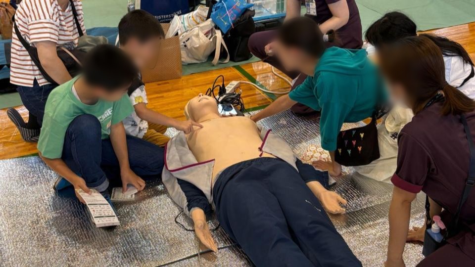 ブースで心肺蘇生の体験に挑戦するこどもたちと、そばで教えるスタッフ